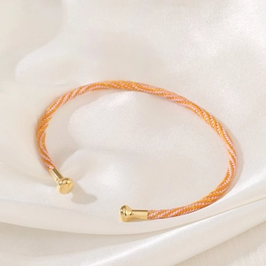 Close-up of pink and orange woven cord bracelet with gold metal end caps on white silk