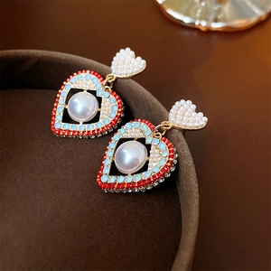 Détail macro de boucles d'oreilles cœur en perles avec strass rouges et bleus sur velours