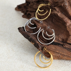 Layered twisted hoop earrings in gold and silver finish on natural wood stand