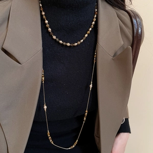 Close-up of layered tiger eye beaded necklace and gold chain on professional model
