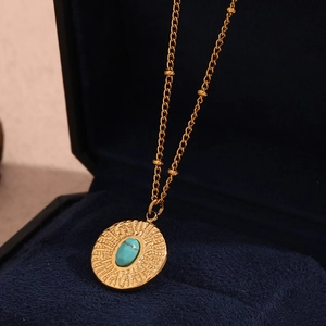 Macro shot of gold hammered turquoise pendant on beaded chain in a blue velvet box