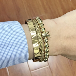 Close-up of three gold-tone stackable bracelets featuring crown charm and woven textures