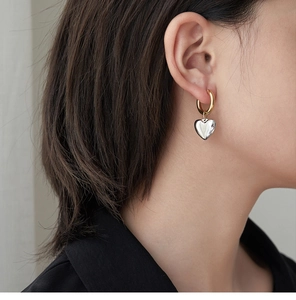 Detailed view of bicolor gold hoop earring with silver heart pendant worn by model