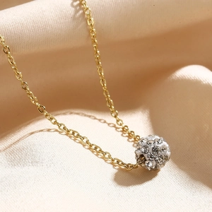 Makroaufnahme einer goldenen Titankette mit glitzerndem Kristallkugel-Anhänger auf Seide