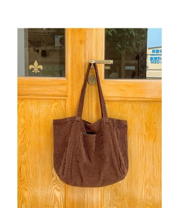 Detailed texture of brown corduroy tote bag hanging on a vintage wooden door handle