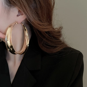 Close-up of a model wearing large gold-plated wide flat hoop earrings with a black blazer