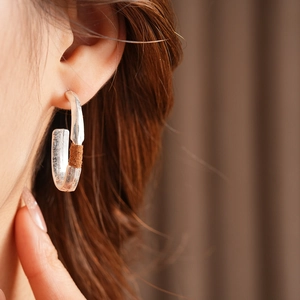 Macro shot of silver C-shaped matte oval earring with brown textured inlay on a model