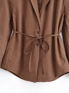 Detailed close-up of brown blazer waist tie design and black button on flat weave fabric
