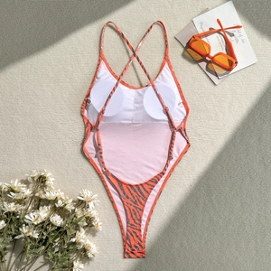 Flat lay of tiger print backless swimsuit with thin straps and orange sunglasses