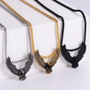 Eagle pendant necklaces in silver, gold, and black steel displayed on geometric blocks