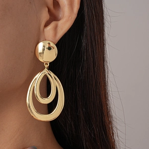Macro shot of minimalist gold double oval metal drop earrings worn by a model