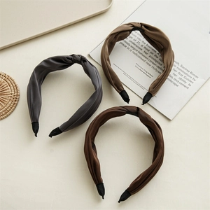 Detail shot of twist knot satin headbands in grey, beige, and brown on a stylish desk