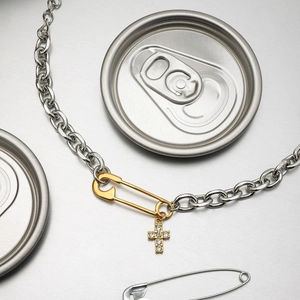 Detailed close-up of mixed-metal paperclip necklace with gold cross and pin pendants