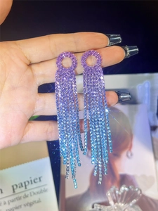 Macro shot of long purple and blue gradient rhinestone tassel earrings in hand