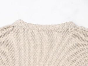 Dettaglio di un maglione in maglia beige con scollo rotondo e morbida trama a maglia grossa