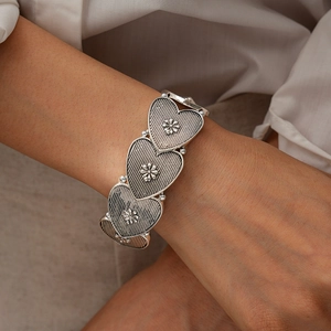Detailed view of vintage silver heart bracelet with embossed flower patterns on model