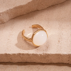 Detail of a gold-plated open ring featuring a white resin stone on a textured stone base