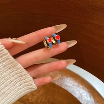 Detail of gold heart earrings with red and blue enamel held in hand for scale