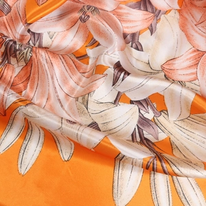 Vibrant orange silk scarf featuring realistic floral lily prints and smooth satin drape
