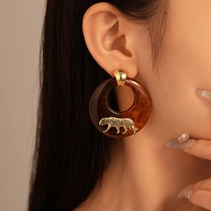 Detail view of retro amber resin ring earrings with gold tiger charms on model