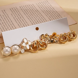 Ten-piece gold flower and faux pearl earring set displayed on a vintage book background