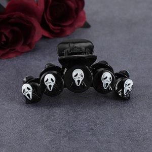 Detail shot of black hair claw clip with five white scream mask motifs on grey background
