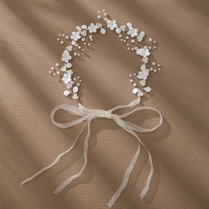 Detail of bridal headband with white ceramic flowers, pearls, and ribbons on brown fabric