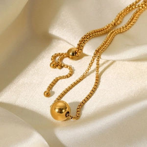 Detailed view of a gold bead pendant necklace on silk fabric with elegant box chain design