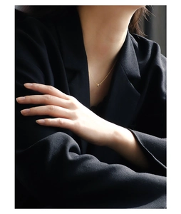 Detail of a minimalist gold necklace with a round zircon pendant worn by a model