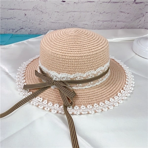 Detail of light beige straw hat featuring white lace trim and brown plaid ribbon bow