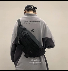 Dettaglio di una grande borsa a tracolla in tela nera con fibbie tattiche su un modello