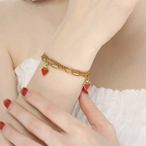 Detail of double-layer gold chain bracelet with red strawberry charms on wrist
