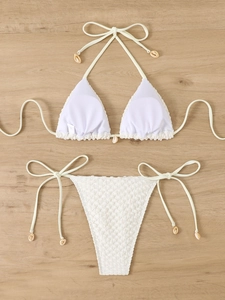 Flat lay detail of white textured bikini set featuring natural seashell charms on ties