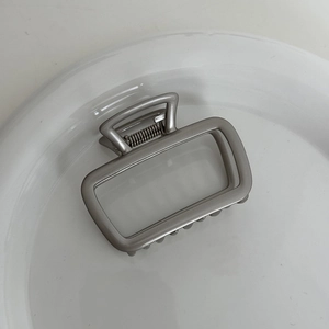 Detailed close-up of a large silver metal bow claw clip in a white ceramic dish