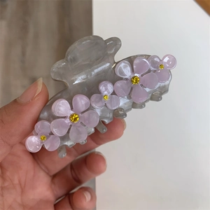 Detail of grey acetate hair claw clip featuring five purple flowers with yellow rhinestones