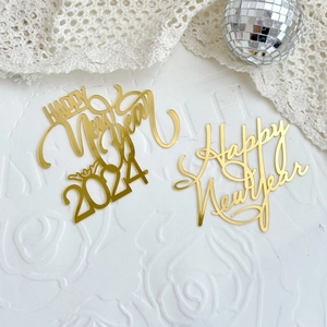 Macro detail of gold Happy New Year 2024 acrylic cake toppers on a lace background