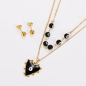 Detail view of double-layer gold necklace and stud earrings with black heart evil eye design