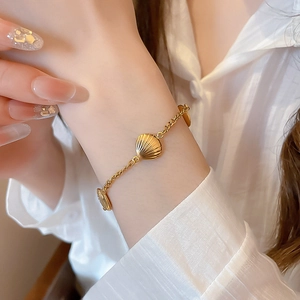 Detailed close-up of a gold stainless steel bracelet featuring shell charms on a wrist