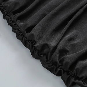 Dettaglio macro del tessuto nero lucido con pieghe elasticizzate per un abito da festa