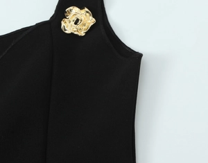 Dettaglio ravvicinato di un top nero in maglia a coste con un ciondolo in metallo a rosa dorata