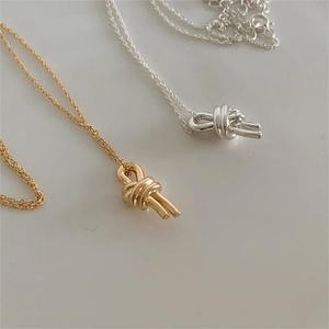 Close-up of minimalist knot pendant necklace in polished gold and silver finishes