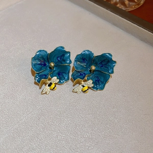 Detailed macro view of blue enamel flower earrings with golden bee and petal accents