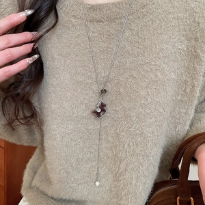Détail d'un collier long argenté avec pendentif poney marron et perle blanche pour femmes