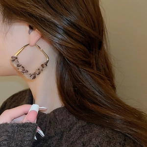 Close-up of model wearing large gold square earrings with leopard print leather detail