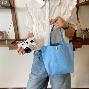 Blue canvas lunch bag with metal snap button closure held by a model in a minimal setting