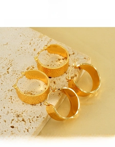 Détail de boucles d'oreilles créoles en acier titane doré avec textures martelées et polies