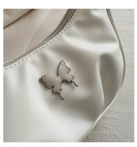 Detailed macro view of a silver butterfly buckle on soft white pleated PU leather bag