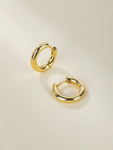 Detail of polished gold stainless steel hoop earrings on textured beige surface