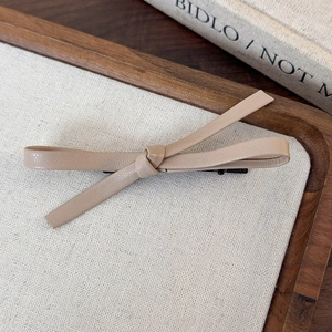 Close-up of beige leather bow hair clip on a wooden tray with a vintage linen texture