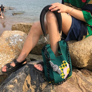 Detail of green canvas handbag with floral checkerboard pattern and chunky black chain strap